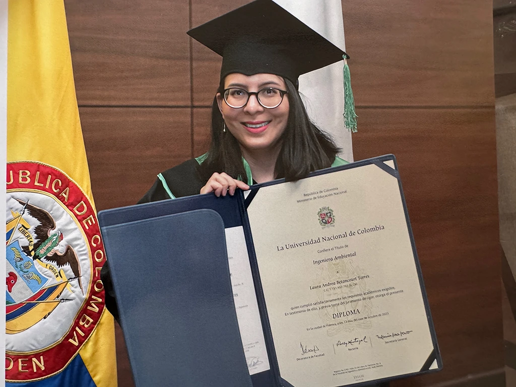 Imagen de la graduación de Laura Andres, quien está posando con su diploma de la Universidad.