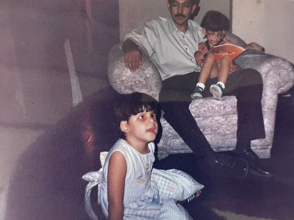 Padre de las hermanas sentado en un sillón con Laura Andrea en su regazo mientras ve de lejos a María Paula sentada en una alfombra.