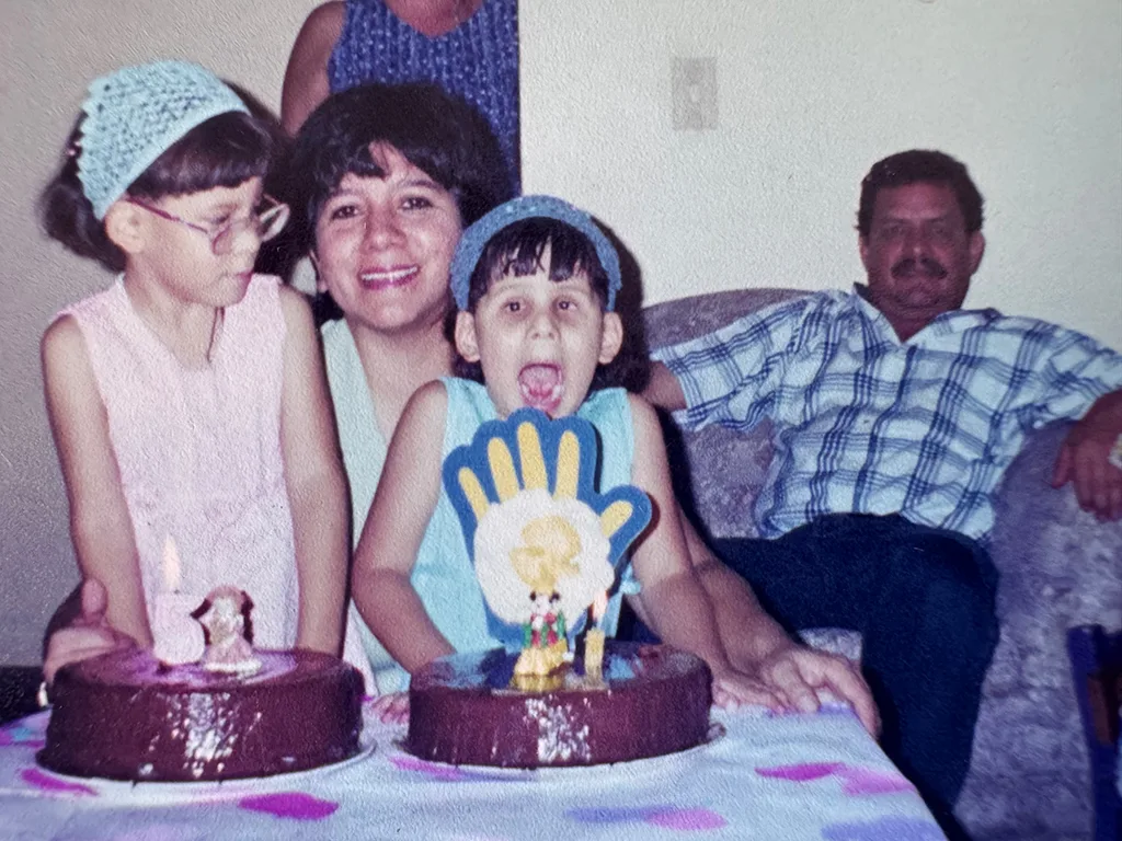Foto de las hermanas celebrando su cumpleaños número 5 con dos pasteles. Madre las acompaña posando en la foto mientras el padre está sentado unos centímetros atrás.